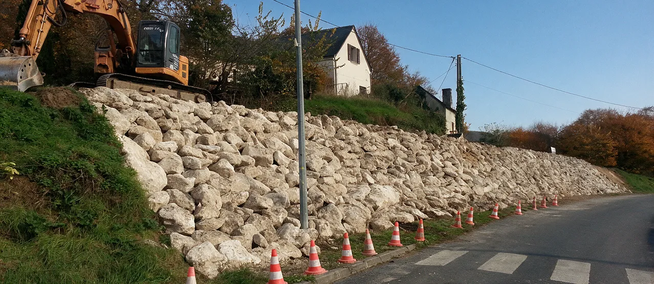 Terrassement et construction de mur en pierres sèches par un engin de chantier près d'une route